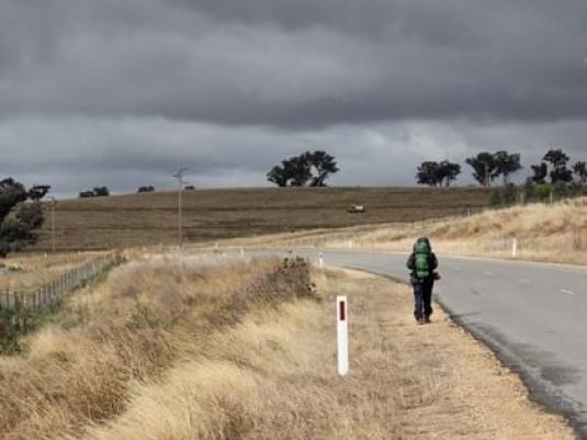 person with backpack on walking down deserted rural road