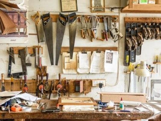 woodworking tools in workshop including saws, hand drills, chisels, planes, squares, design drawings, shelves and workbench
