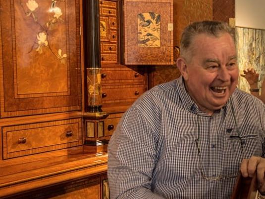 Geoff Hannah in front of the cabinet he crafted. Cabinet has inlays of timber and stone with many drawers and doors