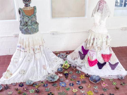 two sculptures of women in skirts surrounded by ceramic flowers on the floor