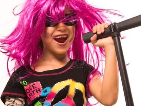child in pink wig and sunglasses rocking out with microphone in hand