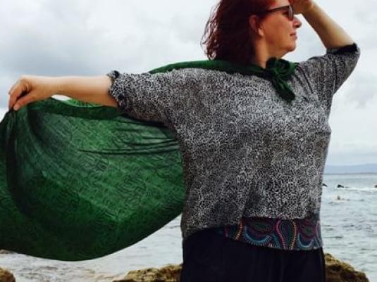 woman looking out to sea with holding a green cape with a rock and sea behind her