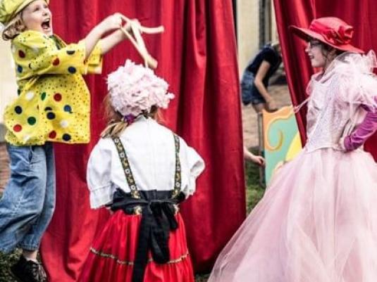 three children in dress-up costumes in front of red curtain