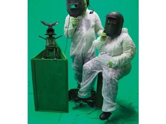 two people in safety suits wearing welding goggle looking at a contraption in front of them