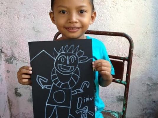 a child on a chair showing the viewer their artwork