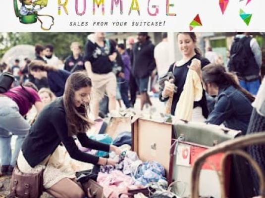 crowd of people at rummage sale with woman in the foreground crouched down looking through clothes in a suitcase