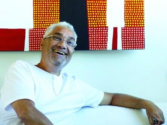 Michael Philp sitting on a couch  in front of one of his colourful paintings