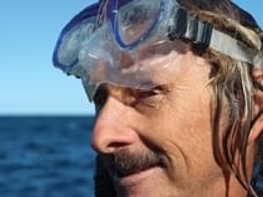 man wearing snorkelling goggles with the sea behind him