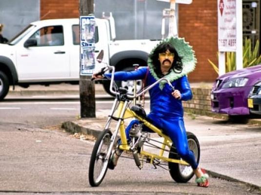 man in blue suit with large green collar siding bike with high handlebars