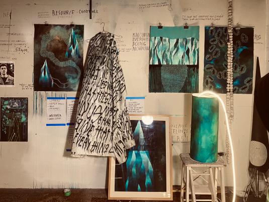 An artist studio with a variety of creative outputs - collage, costume, notes. The colours are white, back and green.