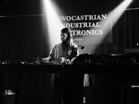 A black and white photo of a man with long hair on a stage playing electronic music