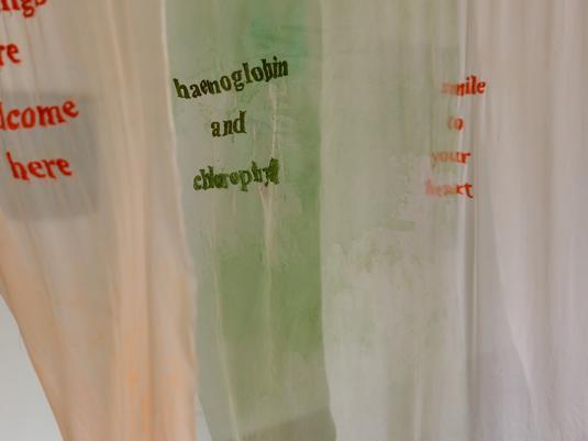 3 banners of sheer material with words embroidered on them. The colours are orange and green.