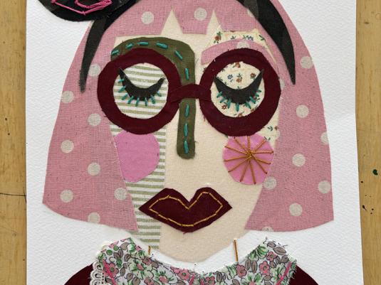 An artwork made from pieces of colurful fabric, creating a portrait of a woman with pink polka dot hair, maroon glasses and a magenta and lace dress