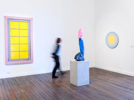 person walking past pink, blue and pink sculpture of a mountain